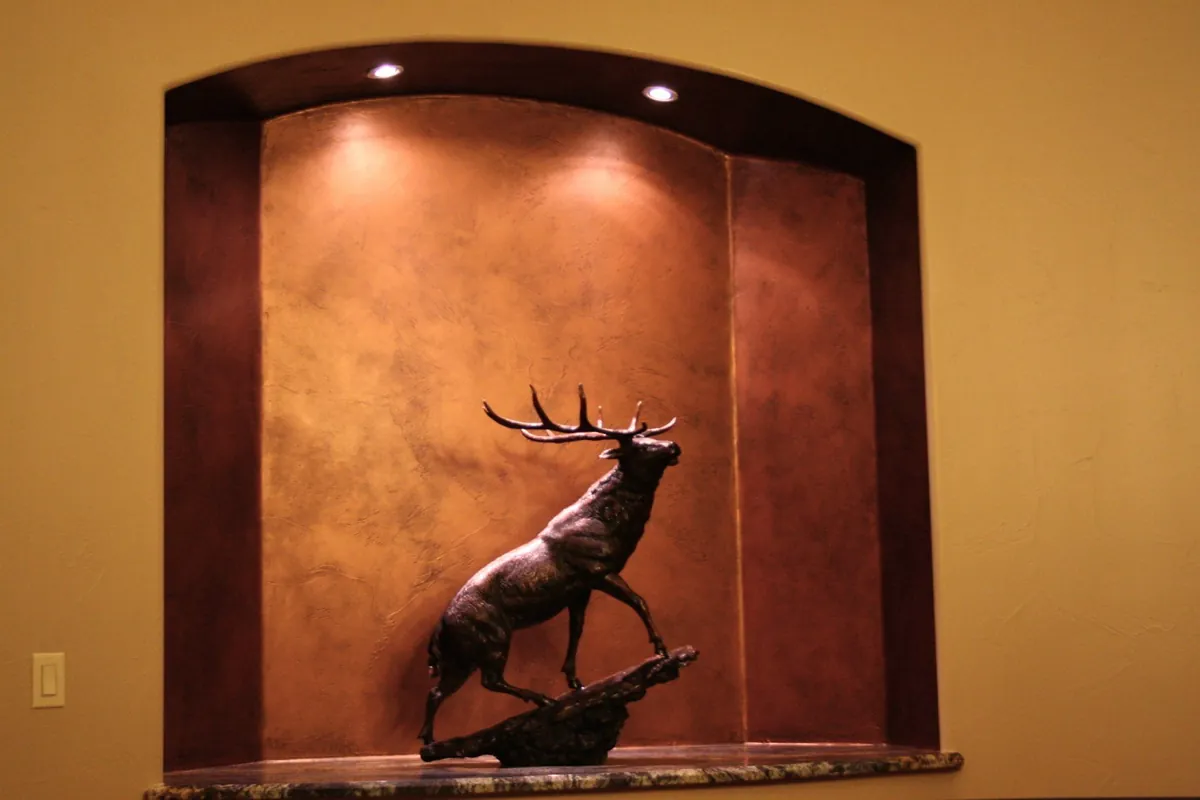 Burnished copper niche lit behind a bronze elk sculpture